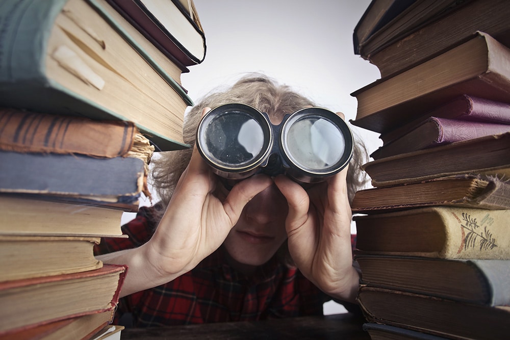 Person blickt mit Fernglas durch Bücher.